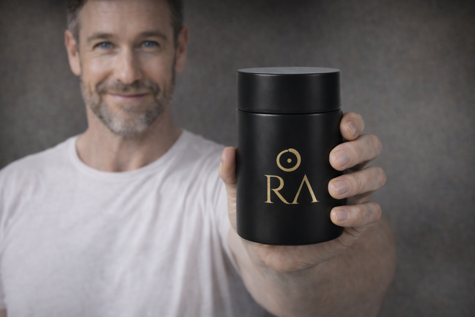 Man holding a black container with 'RA' logo against a gray background